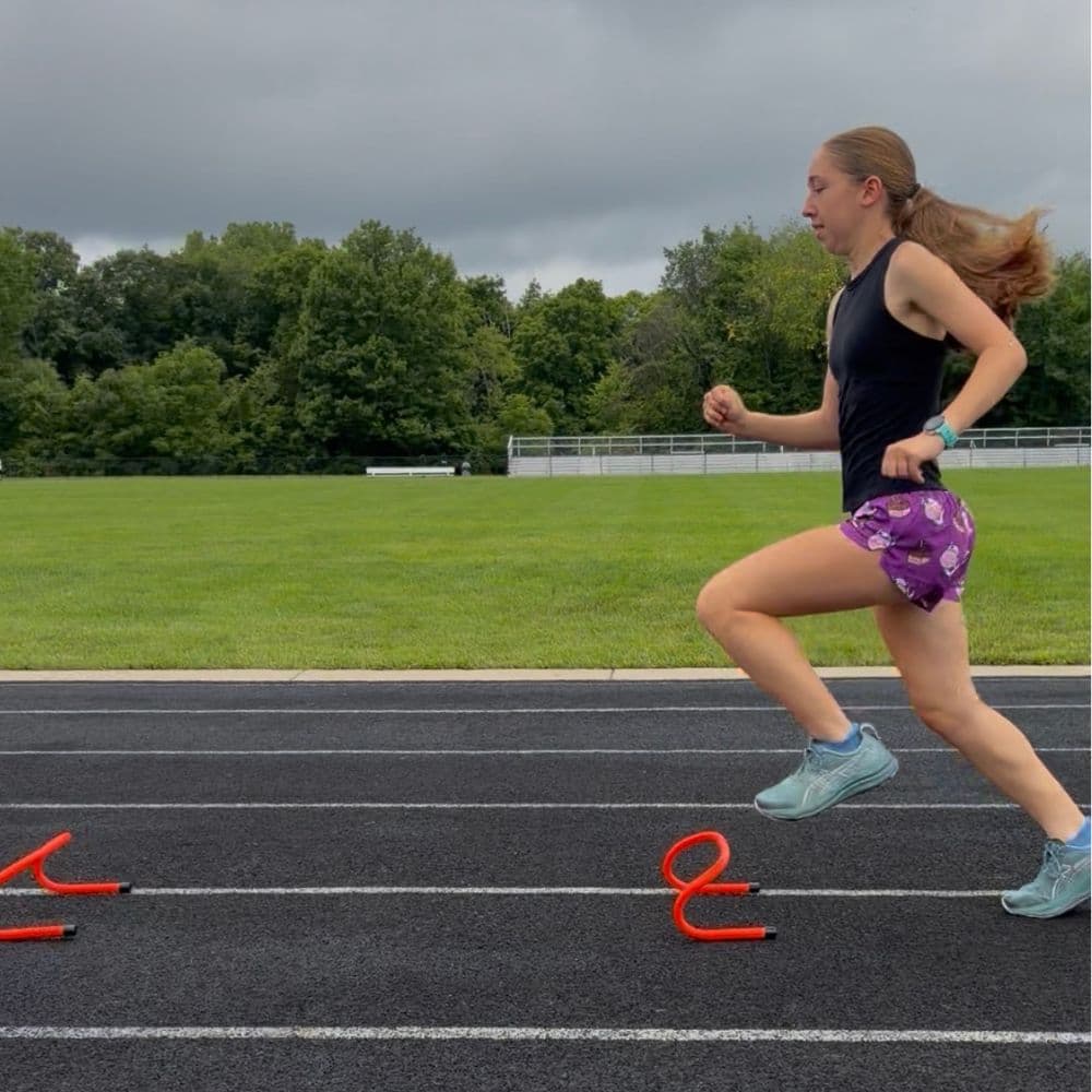 Lucy running sprint mechanics drills over mini hurdles on an outdoor track in Lewis Center, Ohio.